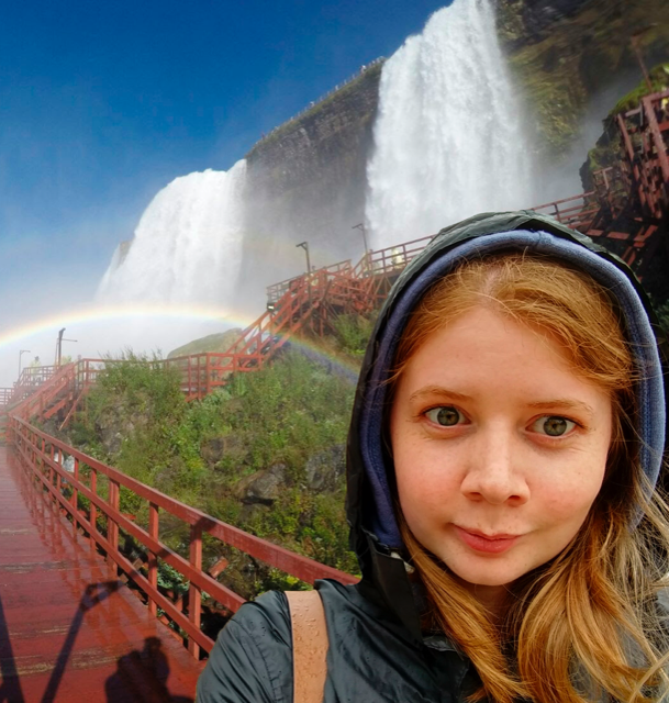 Selfie of a girl wearing a hood. The background has been edited to show a waterfall.