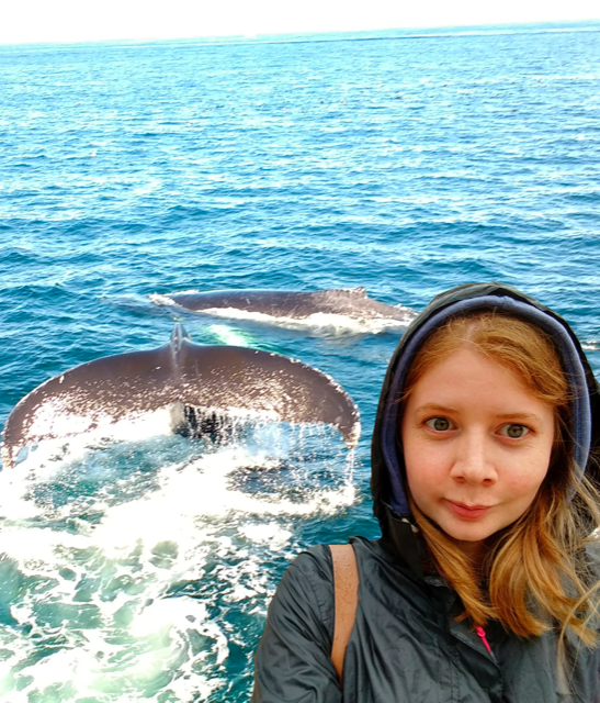 Selfie of a girl in a hood. The background has been edited to show the ocean and some whales.