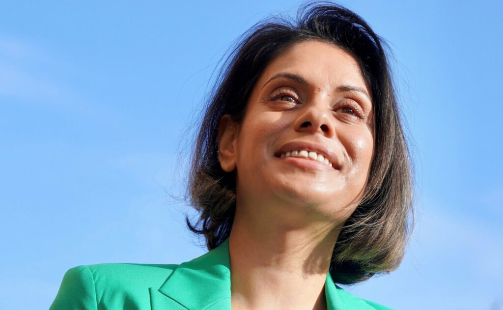 Geena Patel senior communications officer wearing a green jacket and smiling on a sunny day with blue skies