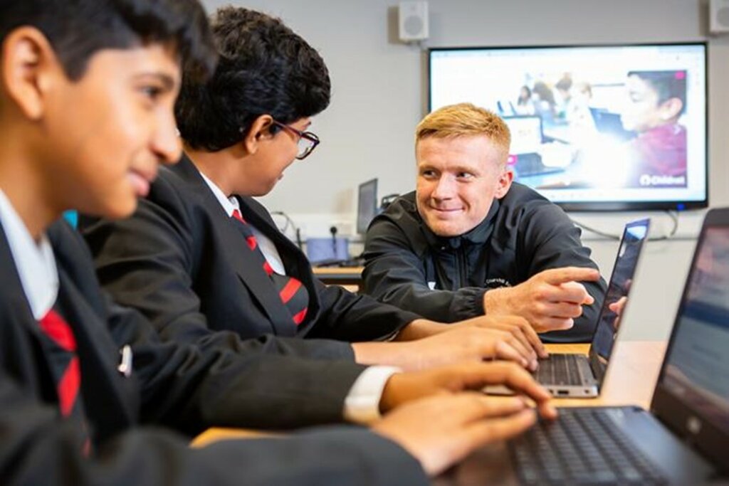 Smiling children working together on the digital leaders online programme with the support of an adult